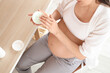 © Pixel-Shot - Young pregnant woman applying cream at home office, closeup