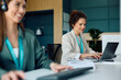 © Drazen - Smiling businesswoman working on laptop in office.