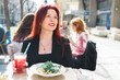 Beautiful happy millennial woman with long red hair enjoying italian pasta in a street cafe