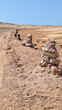 Close up of road in a desert area fenced with homemade pyramids made of stones.Vertical