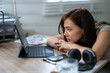© Wasana - A woman is sitting at a desk with a laptop and a cell phone. She is looking at the laptop screen with a sad expression on her face