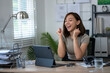 © Wasana - A woman is sitting at a desk with a tablet and a laptop. She is smiling and she is happy