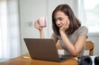 © Wasana - A woman is sitting at a table with a laptop and a pink mug. She is looking at the laptop and she is in a bad mood