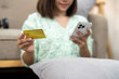 © Wasana - A woman is holding a credit card and looking at her phone. She is smiling and she is happy