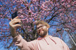 Spring day. Bearded man in pink shirt talking by phone. Spring pink sakura blossom. Handsome young man with smartphone. Fashionable man in trendy glasses. Bearded stylish man. Copy space