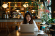 © aamulya - Young woman working on a laptop while sitting in coffeeshop