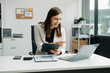 © laddawan - Confident business expert attractive smiling young woman typing laptop and holding digital tablet