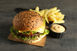 Burger with delicious patty, french fries and sauce on gray table