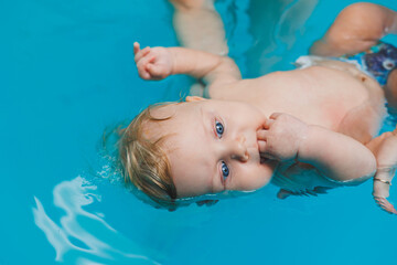 Wall Mural - A 2-year-old little boy learns to swim in a pool with a coach. Swimming lessons for children