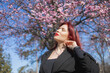 Fashion outdoor photo of beautiful woman with red curly hair in elegant suit posing in spring flowering park with blooming cherry tree. Copy space and empty place for advertising text