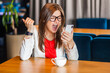 Portrait of angry aggressive business woman in glasses sitting at table having video call on smart phone screaming with hate negative feelings. Indoor shot, cafe or office background.