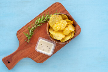 Wall Mural - Homemade potato chips over background of wooden board with tartar sauce and rosemary branch.