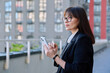 Mature business woman using smartphone, modern city background