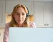 Woman Wearing Headset Working From Home In Kitchen Using Laptop