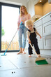 Mother With Young Son At Home In Kitchen Helping With Housework Sweeping Floor