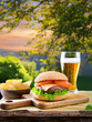 Close-up view of a fresh burger with lettuce, cheese, and tomato, a glass of beer, and a bowl with potato chips on the side. Outdoors, blurry trees and bushes foliage, sunset.