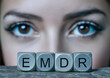 Eye Movement Desensitization and Reprocessing Psychotherapy Treatment concept. Letters EMDR written on grey cubes. Close-up woman's face with eyes wide open. 