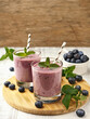 Two glasses of blueberry smoothie on a round wooden board. Some berries on the table.