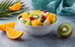 A bowl of healthy colorful tropical fruit salad. On the side quartered oranges and a halved kiwifruit.  Healthy eating concept. 
