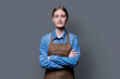 Portrait of young smiling confident woman in apron on grey background