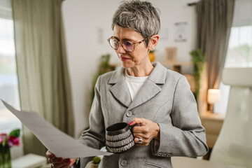 Portrait of mature woman stand and hold cup and document at office