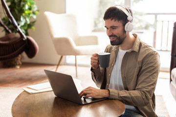 Aufkleber - A man is seated at a table, focused on his laptop screen. Next to him is a cup of coffee, steam rising. The mans hands are typing on the keyboard as he works.