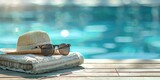 Fototapeta Motyle - A towel with sunglasses and a straw hat on a wooden table with blue swimming pool background,