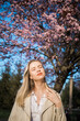 Fashion outdoor photo of beautiful woman with blond hair in elegant suit posing in spring flowering park with blooming cherry tree. Copy space and empty place for advertising text