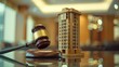 A small wooden gavel and miniature model of an apartment building on a glass table with a blurred background
