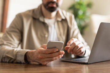 Aufkleber - Cropped of man is sitting at a table while actively using a cell phone. He appears engaged with the device, possibly texting, browsing, or talking on the phone.