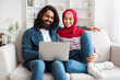 © Prostock-studio - Bright and airy shot of a young eastern couple using a laptop together, showcasing a moment of daily life in their modern living room