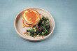 Traditional American pancakes with spinach, pine-nuts and raisins served as close-up on a Nordic design plate