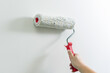 A woman's hand paints a wall white with a paint roller