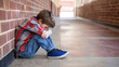 © Luluraschi - sad and bullied middle school boy student sitting on the hallway floor by himself, head down, outcast