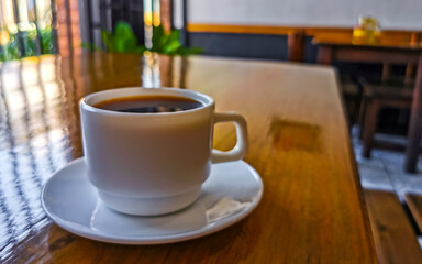 White cup of black Americano coffee on a wooden table.