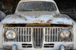 Front close up of a white abandoned old car with half open hood 