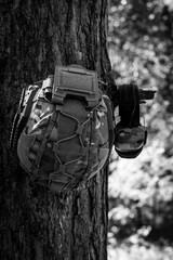 Wall Mural - A tactical helmet and active tactical headphones hang on a tree branch. Defense of the military, military operations. War in Ukraine.
Black and white photo.