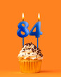 Blue candle number 84 - Birthday cupcake on orange background