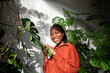 Happy black woman among green home garden stroking holding plants leaves. Portrait, smiling laughing cheerful african american girl joyfully looking at camera against sunny greenhouse urban jungle.