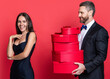 Loving man giving present gift box for Valentines day to surprised woman. Man receiving present. Happy Valentines day. Couple in love isolated on red. Birthday couple with gift