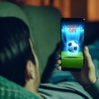 A man lying on a cozy sofa, watching a live soccer match on his smartphone