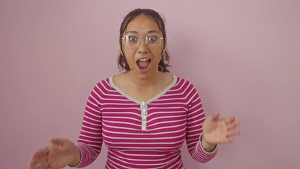 Poster - Young hispanic woman, scared and astonished, stands wearing a stripes t-shirt over a pink isolated background, her mouth gaping with an amazed look of disbelief on her face.