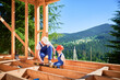 Father with toddler son building wooden frame house. Male builder demonstrating to his son how to measure level using spirit level on construction site on sunny day. Carpentry and family concept.