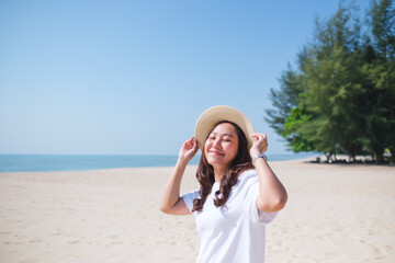 Wall Mural - Portrait image of a beautiful woman holding hat while strolling on the beach