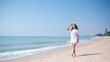 Portrait image of a young woman while strolling on the beach with the sea and blue sky background