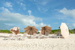 A row of empty beach loungers and toppled umbrellas on a white s