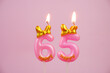 Pink birthday candle with bow and word happy burning on pink background., number 65.
