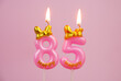 Pink birthday candle with bow and word happy burning on pink background., number 85.