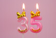 Pink birthday candle with bow and word happy burning on pink background., number 35.