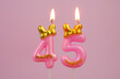 Pink birthday candle with bow and word happy burning on pink background., number 45.
